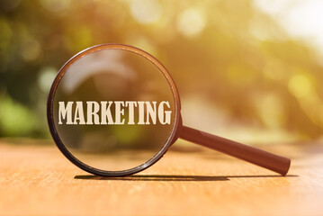 A magnifying glass enlarges the word MARKETING set against a warm, blurred backdrop.
