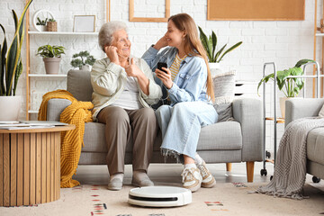 Senior woman and her granddaughter listening to music together with robot vacuum cleaner at home