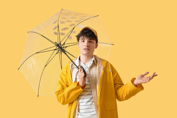Young man in raincoat with umbrella on yellow background