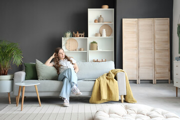 Young woman sitting on grey sofa in living room