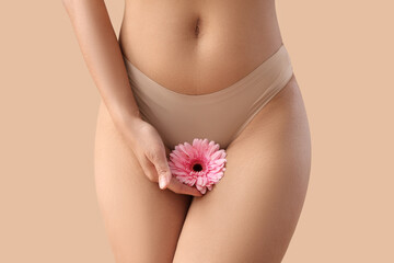 Beautiful young woman in panties with gerbera flower on beige background, closeup