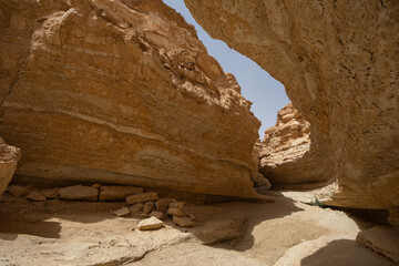 Fototapeta premium Narrow winding path cutting through heart of Tamaghza canyon, flanked by tall layered rock walls under hot Tunisian sun