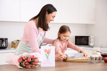 Happy mother with her cute little daughter rolling out dough in kitchen on holiday
