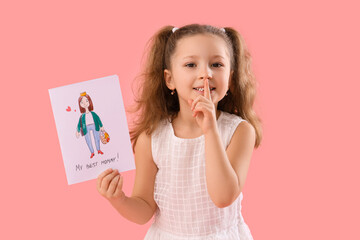 Cute little girl with card for Mother's Day showing silence gesture on pink background