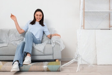 Young woman with rolled carpet sitting in room on moving day