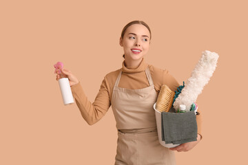 Young woman holding spray bottle and bucket with cleaning supplies on beige background
