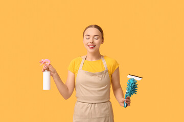 Pretty young woman with cleaning supplies on orange background
