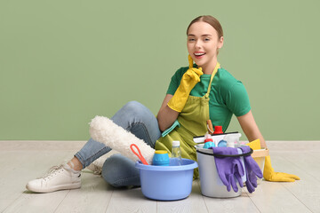 Young woman different cleaning supplies sitting on floor near green wall