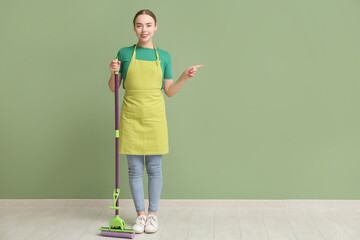 Young woman with floor mop pointing at something near green wall