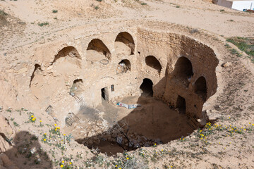 Abandoned Berber dwellings with arched doorways carved into walls of earthen pit in Matmata,...