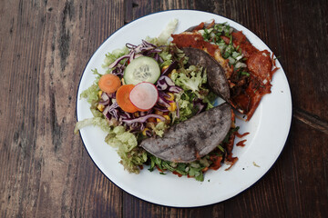 A delicious plate featuring two tacos and a side of fresh salad. The tacos are filled with savory ingredients and wrapped in blue corn tortillas.