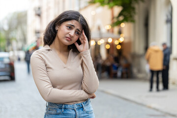 Sad unhappy Indian young woman thinks over life concerns suffers from unfair situation outdoors. Problem feeling bad annoyed burnout grief. Hispanic girl alone on urban city street. Town lifestyles