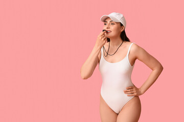 Female lifeguard with whistle on pink background