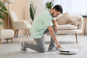 Young man turning on modern robot vacuum cleaner at home