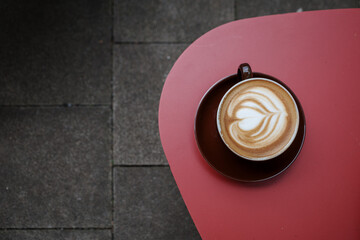 A beautifully crafted latte with heart-shaped latte art, served in a brown cup and saucer, placed...