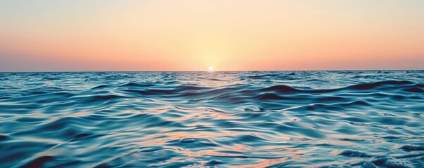 Obraz premium Calm ocean waves at sunset with a clear sky above. The serene water reflects the soft pastel hues of the setting sun, creating a peaceful and tranquil seascape.