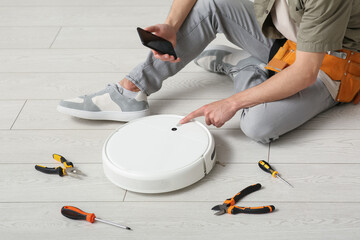 Man with tools and mobile phone fixing modern robot vacuum cleaner at home