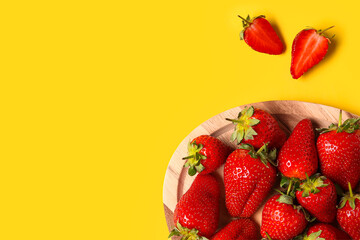 Wooden board with sweet fresh strawberries on yellow background