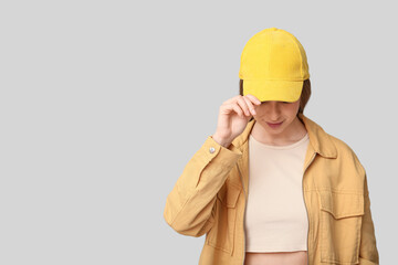 Beautiful young woman in stylish yellow cap on grey background