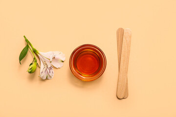 Glass bowl with sugaring paste, alstroemeria flower and wooden sticks on yellow background
