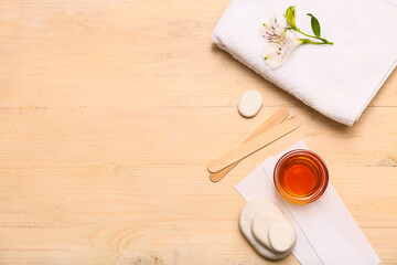 GLass bowl with sugaring paste, wax strips, sticks, spa stones and alstroemeria flower on light wooden background