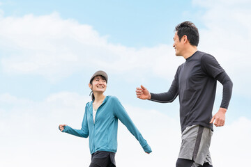 公園で話しながらウォーキング・ジョギング・トレーニングするスポーツウェアを着たアジア人の男女（話す）
