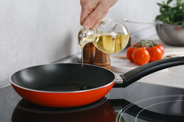 Vegetable fats. Woman pouring cooking oil into frying pan on stove in kitchen, closeup