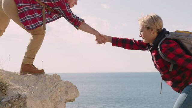 Woman lends helping hand to friend while climbing to top of mountain in travel. 