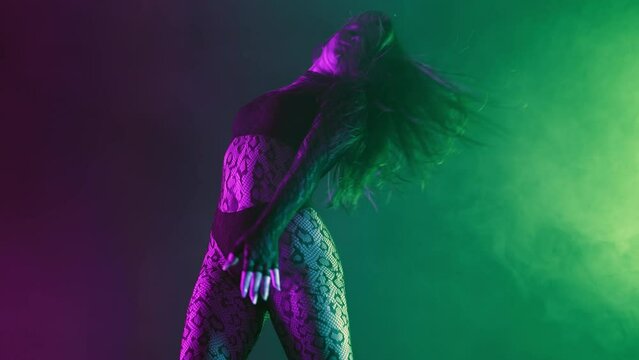 Seductive young woman sexually moving body, long hair, hips in colorful light. Erotic private dance in night club with neon. Lady dancer in tight lace clothes and heels.