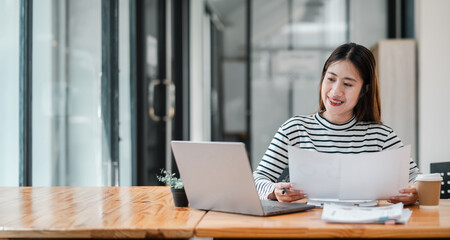 A woman is sitting at a desk with a laptop and a stack of papers. She is smiling and she is enjoying her work