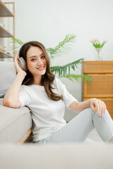 A woman is sitting on a couch with her headphones on. She is smiling and she is enjoying her music