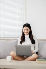A woman is sitting on a couch with a laptop in front of her. She is smiling and she is enjoying her time