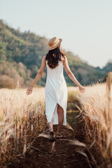 A woman wearing a straw hat walks through a field of tall grass. She is enjoying the outdoors and the peacefulness of the scene