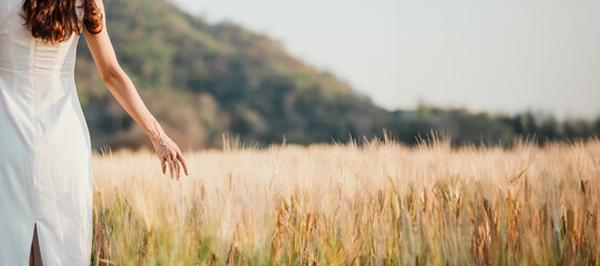 A woman is walking through a field of tall grass. The field is empty and the sky is clear. The woman is wearing a white dress and she is enjoying the peacefulness of the field