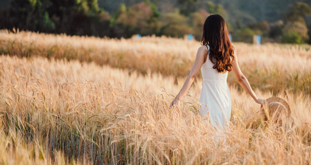 A woman is walking through a field of tall golden wheat. She is wearing a white dress and a straw hat. The scene is peaceful and serene, with the woman enjoying the beauty of the natural landscape