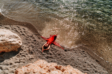 Woman red dress sea. Female dancer in a long red dress posing on a beach with rocks on sunny day