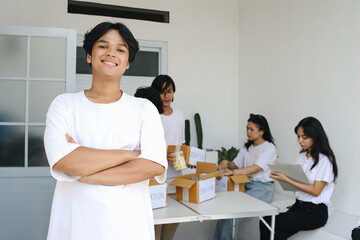 Smiling Young Asian Man With Other Community Members Packing Food for Charity Event on The Background
