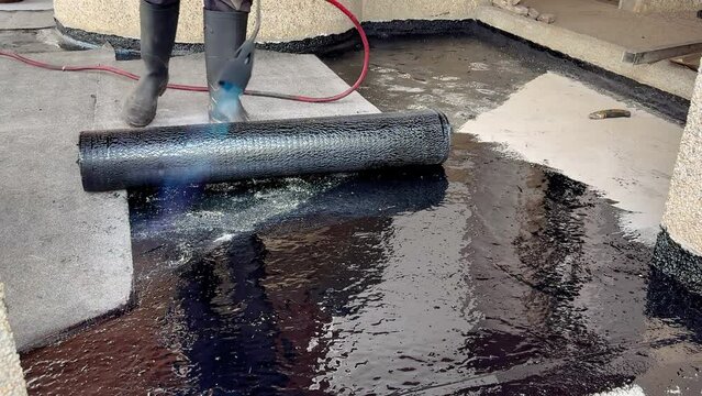 Construction worker heating with a blow torch an bituminous material and rolled across a concrete surface