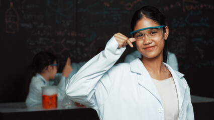 Highschool girl looking at camera while people doing experiment at laboratory. Young cute student...
