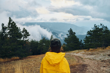 A person in a vibrant yellow raincoat on a majestic hill admiring stunning mountain peaks and fluffy clouds