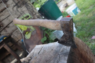 Used Ax hatchet stuck in a wood stump, in courtyard, countryside area