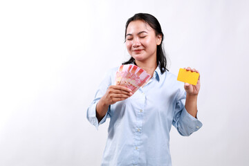 Happy asian woman holding credit card and Indonesian money rupiah, smiling, posing against white studio background