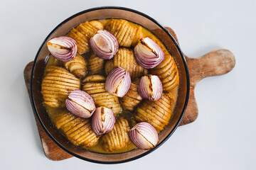 plant-based roasted hasselback potatoes with onions in round oven tray