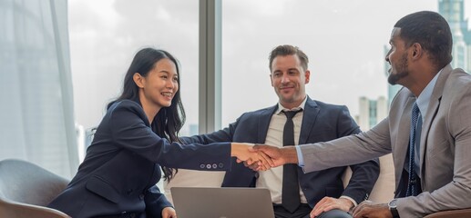 A diverse group of business professionals in suits shaking hands in an office.