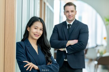 A professional headshot of a man and a woman in business suits, smiling at the camera with crossed arms.