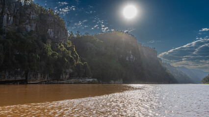 A red-brown exotic river with steep banks. Green vegetation on the sheer limestone slopes. The sun...