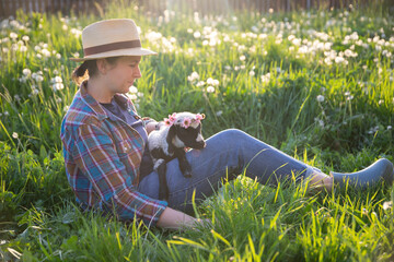 Cheerful woman with a hat sitting in green grass, holding a cute little lamb