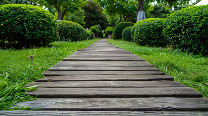 Fototapeta premium Straight wooden walkway in the park with green lawn, trees and bushes, landscape design