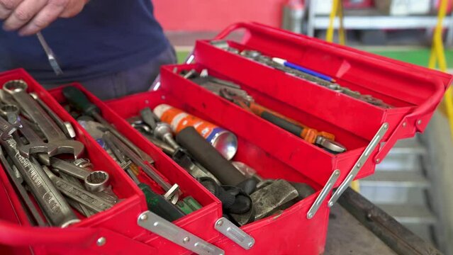 Caja de herramientas roja abierta por un obrero, saca una llave ingles y vuelve a cerrarla. Trabajador