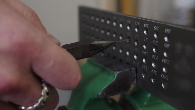 A person is using a pair of pliers to open a small box with a bunch of small hol